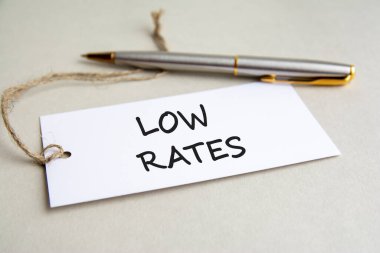 Metin içeren beyaz kart Gri arkaplanda metal kalemle düşük oranlar.