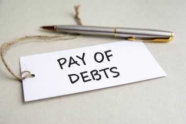 Borçların yazılı olduğu beyaz kart ve gri arka planda metal kalem.