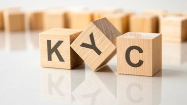 Gri bir masanın parlak yüzeyinde KYC harfleri olan üç tahta küp. Küplerdeki yazıtlar masanın yüzeyinden yansıyor. İş konsepti. kyc - müşterinizi tanıyın
