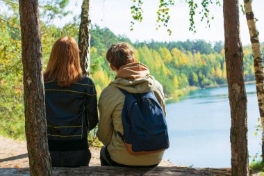 Romantik çift sonbahar parkında dinleniyor, sarılıyorlar, temiz havanın tadını çıkarıyorlar, güzel doğa, güzel sonbahar havası. Sevgililer birlikte vakit geçirir. Dikiz aynası. Sarı yapraklar, arka planda göl