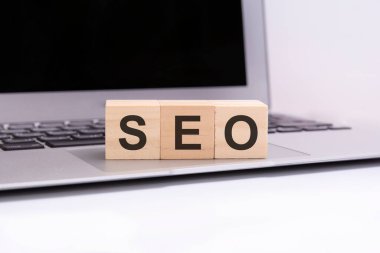 SEO - gümüş dizüstü bilgisayar klavyesinde harfleri olan tahta küpler. SEO - Arama Motorları optimizasyonunun kısaltılmışı. Harflerle ahşap elementlerin toplandığı iş kavramsal sözcükleri.