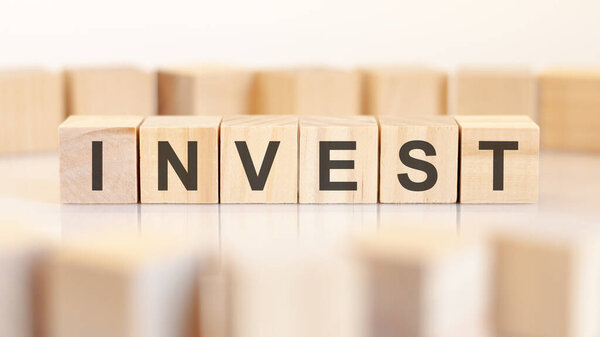 Слово invest написано на деревянных кубиках, стоящих в ряд. вокруг блоков с буквами на светлом фоне. могут быть использованы для бизнес и финансовых концепций. селективный фокус.