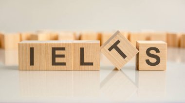 ielts. Gri arka planda harfleri olan tahta blokların sözleri. Masanın aynalı yüzeyindeki başlığın yansıması. seçici odak.