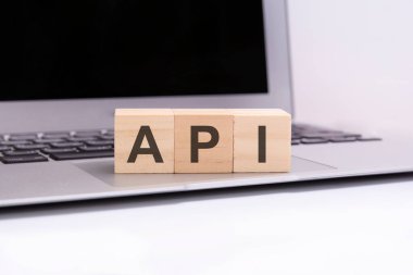 API - gümüş dizüstü bilgisayar klavyesinde harfleri olan tahta küpler. API - uygulama programlama arayüzünün kısaltması. Harflerle ahşap elementlerin toplandığı iş kavramsal sözcükleri.