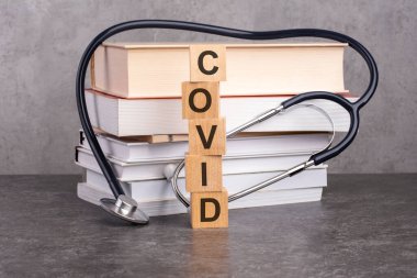 Covid kelimesi, kağıt bir arka planda steteskopun yanındaki tahta küplere yazılır. Kitap ve steteskopla tıp eğitimi kavramı.