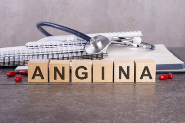 Covid-Angina metninin yeni versiyonu gri bir masanın üzerinde duran tahta bloklardan oluşuyor. Arka planda yazı ve tabletler için bir yığın kağıt defter var..