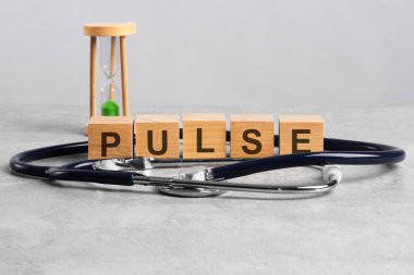 Tahta blok, doktorun masasında steteskop ve kum saati ile Pulse kelimesini oluşturur. Tıbbi konsept: Açık gri gergedan. Hastane, klinik ve tıp sektörü için sağlık hizmetleri kavramı.