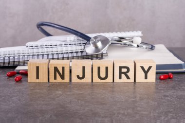 Yaralı - metin gri bir masanın üzerinde duran ahşap bloklardan oluşur. Arka planda yazı ve tabletler için bir yığın kağıt defter var. tıbbi konsept, gri arkaplan