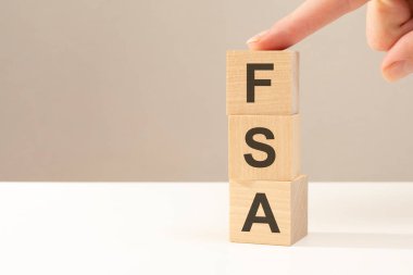 El, FSA harfinin yanına tahta bir küp koyuyor. Finansal Güvenlik Sigortası 'nın kısaltması. İş konsepti. Soldaki metin için boşluk. ön görünüm