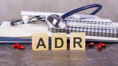 ADR kelimesi, kağıt arka planda steteskopun yanındaki tahta küplere yazılır. Tahta elementlerin harflerle toplandığı tıbbi kavramsal kelime. ADR - Ters Uyuşturucu Reaksiyonunun kısaltılmışı