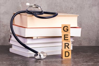 GERD kelimesi, gri arka planda steteskopun yanındaki tahta küplere yazılır. Hastane, klinik ve tıbbi işler için tıbbi konsept. Kitap ve steteskopla tıp eğitimi kavramı