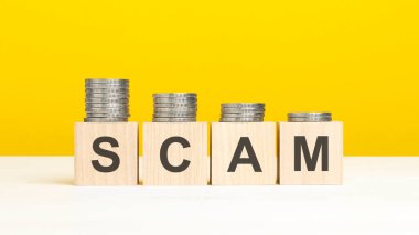 Ahşap blok üzerine yazılmış SCAM metni, sarı arka planda istiflenmiş paralar, bsibess konsepti