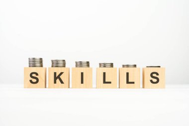 Tahta blok üzerine yazılmış SKILLS metin beyaz arka planda istiflenmiş madeni paralar, iş konsepti