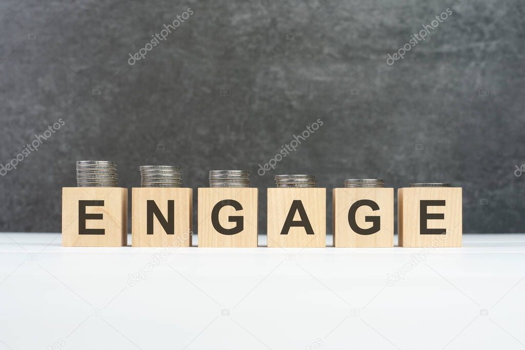 ENGAGE word, text written on wooden cubes with stacks of coins of different heights on each cube on a black background, business concept