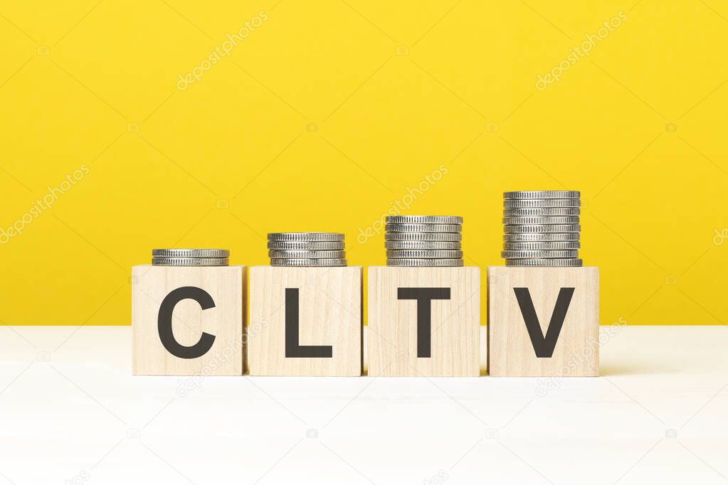 CLTV text written on wooden block with stacked coins on yellow background, business concept. CLTV - short for Customer Life Time Value.