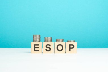 ESOP konsepti. Tahta sehpanın üzerinde yazı ve bozuk paralar olan tahta bloklar. kopyalama alanı. mavi arka plan. ESOP - çalışanların hisse senedi sahipliğinin kısaltılmışı