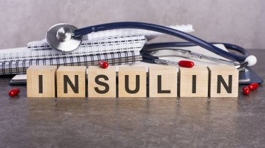 INSULIN - metin gri bir masanın üzerinde duran ahşap bloklardan oluşur. Arka planda yazı ve tabletler için bir yığın kağıt defter var. tıbbi konsept, gri arkaplan