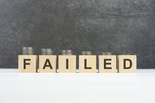 failed word, text written on wooden cubes with stacks of coins of different heights on each cube on a black background, business concept