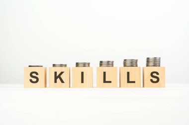 Tahta blok üzerine yazılmış SKILLS metin beyaz arka planda istiflenmiş madeni paralar, iş konsepti