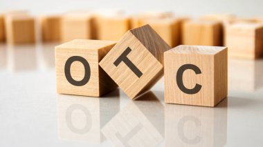 Gri bir masanın parlak yüzeyinde OTC harfleri olan üç tahta küp. Küplerdeki yazıtlar masanın yüzeyinden yansıyor. OTC - Tezgahın Üzerinde 'nin kısaltılmışı