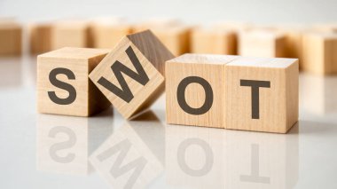 Gri bir masanın parlak yüzeyinde SWOT harfleri olan dört tahta blok. Küplerdeki yazılar yüzeyden yansıyor. SWOT - Güçlü ve Zayıf Fırsatlar Tehditleri 'nin kısaltması