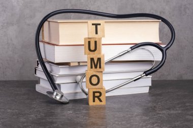 TUMOR kelimesi, kağıt bir arka planda steteskopun yanındaki tahta küplere yazılır. Kitap ve steteskopla tıp eğitimi kavramı