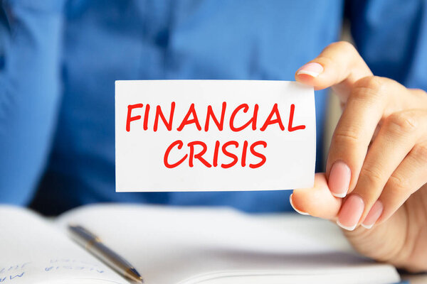 FINANCIAL CRISIS is written on a white business card in a woman's hand. Blue background. Business and advertising concept