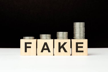 Beyaz masada üzerinde harfler olan dört tahta küp var. Sahte kelime. Siyah arkaplan ve artan bozuk para yığını. ön görünüm