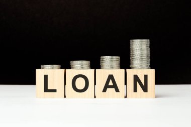 Beyaz masada üzerinde harfler olan dört tahta küp var. Ödünç kelime. Siyah arkaplan ve artan bozuk para yığını. ön görünüm