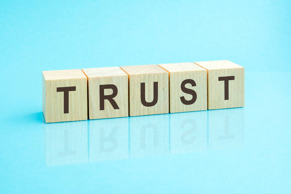 Trust - word written on wooden blocks. text is written in black letters and is reflected in the mirror surface of the table, blue background. business concept for your design