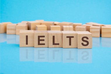 Mavi bir masanın parlak yüzeyinde IELTS harfleri olan tahta bloklar. Küplerdeki yazılar yüzeyden yansıyor. IELTS - Uluslararası İngilizce Test Sistemi 'nin kısaltması