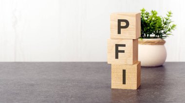 Ahşap küplere, yeşil bitkilere, beyaz arka plana PFI alfabesinin harfleri. PFI - Özel Finans Girişimi 'nin kısaltması