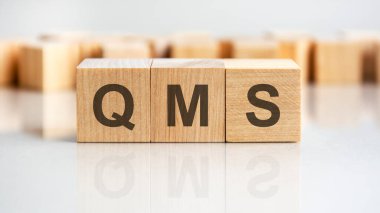 Gri arkaplandaki tahta küplere QMS konsepti. Finansal, ticari ya da ekonomik temalı bir yazı. QMS - Kalite Yönetim Sistemi 'nin kısaltması
