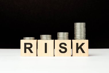 Beyaz masada üzerinde harfler olan dört tahta küp var. Riskli kelime. Siyah arkaplan ve artan bozuk para yığını. ön görünüm.