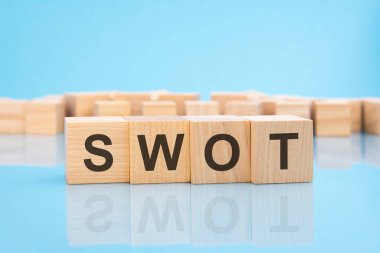 Mavi arka planda tahta küplerde SWOT kelimesi var. Küplerdeki yazılar yüzeyden yansıyor. İş konsepti. SWOT - Güçlü ve Zayıf Fırsatlar Tehditleri 'nin kısaltması