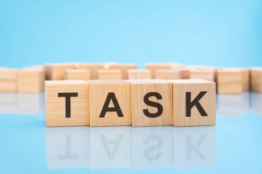 Mavi arka planda tahta küplerle ilgili kelime TASK. Küplerdeki yazılar yüzeyden yansıyor. iş kavramı
