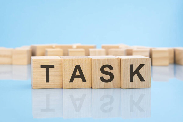 word TASK on wooden cubes on blue background. the inscription on the cubes is reflected from the surface. business concept