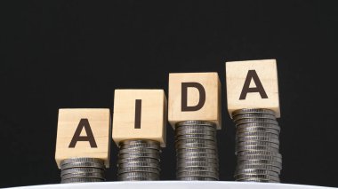 Siyah arka planda sikkeler ve üzerinde Aida, iş ve ekonomi kavramları yazılı tahta küpler var. Aida - ilgiyi üzerine çekmenin kısaltması.