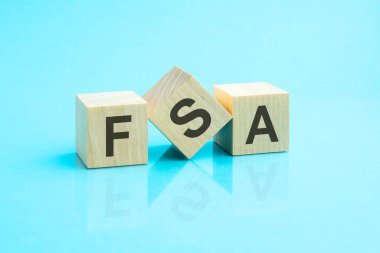 FSA - ahşap blokların kısaltması ve mavi arkaplanda harfler var. Tablonun aynalı yüzeyindeki başlığın yansıması. Seçici odaklanma. FSA - Esnek harcama hesabının kısaltması