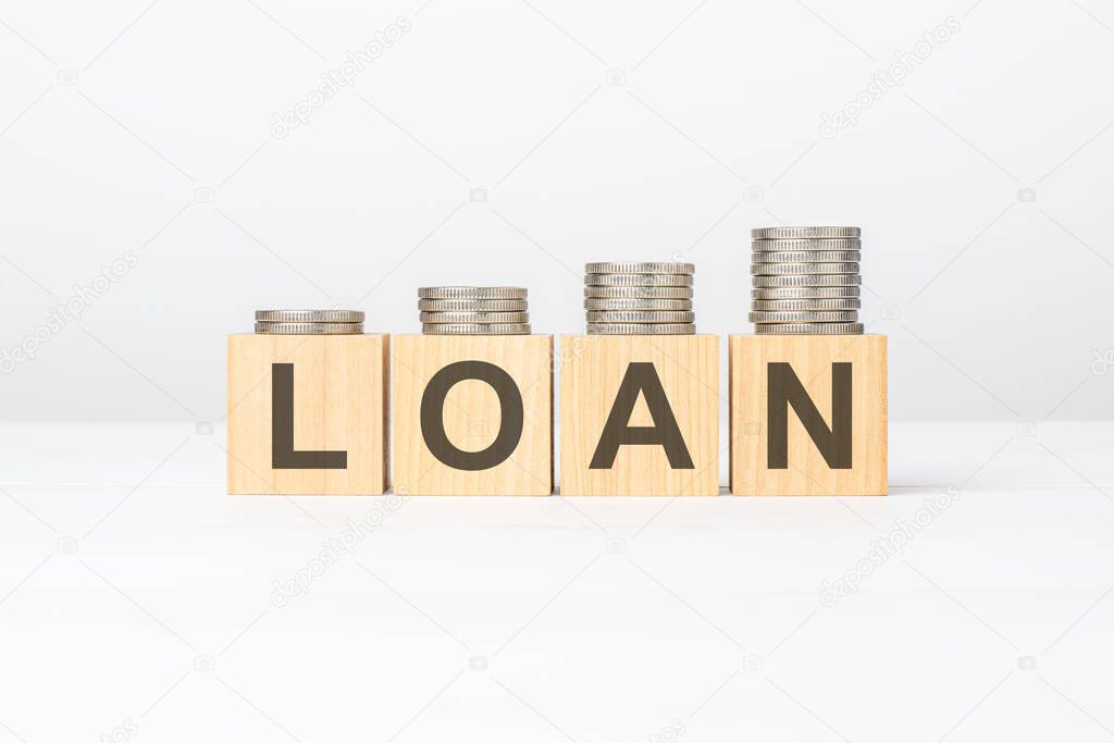 Loan text written on wooden block with stacked coins on white background, business concept