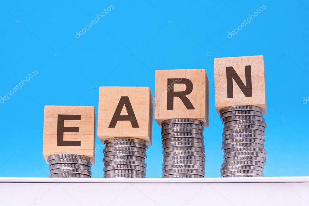 wooden cubes with the word Earn on money pile of coins, business concept, blue background
