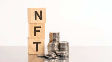 NFT sözcüğü tahtadan küplerden dökülür ve beyaz arka planda bozuk paralarla birlikte harfler bulunur. NFT - karşılanamayan sembol - dijital varlık ile bağlantı kurmak için engelleme teknolojisi kullanan özel bir kripto simgesidir.
