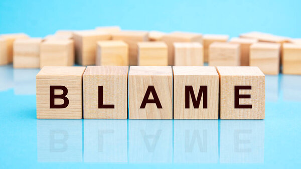 four wooden blocks with the letters blame on the bright surface of a blue table. the inscription on the cubes is reflected from the surface. business conceptual.