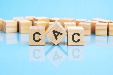 Metin CAC - ahşap küplere siyah harflerle yazılmış, küpler parlak mavi cam bir yüzey üzerinde yer alıyor. konsept kelime arka planda küplerle şekilleniyor. CAC - Müşteri Edinme Maliyetinin kısaltılmışı