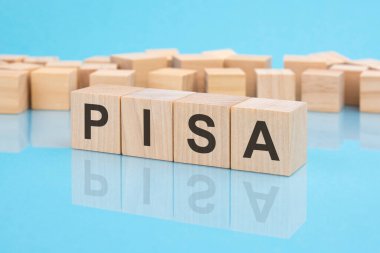 Pisa. Tahta bloklara yazılmış bir kelime. Metin siyah harflerle yazılır ve masanın ayna yüzeyine, mavi arkaplana yansıtılır. Pisa - Uluslararası Öğrenci Değerlendirmesi Programı anlamına gelir