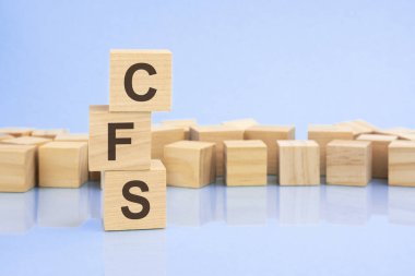 parlak soluk bir leylak ve mavi arka planda, açık tahta bloklar ve CFS yazılı küpler. Küpler yüzeyden yansıyor. cfs - birleşik mali beyanatın kısaltması