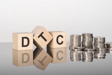 DTC - Doğrudan Tüketiciye - metin, ayna yüzeyinde duran tahta küplerin üzerindeki harflerden oluşur, gri arkaplan. Bozuk paralarla dolu desteler. Yazı yüzeyden yansıtılır. seçici odak.