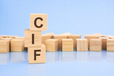 parlak soluk bir leylak ve mavi arka planda, açık tahta bloklar ve CIF yazılı küpler. Küpler yüzeyden yansıyor. CIF - Maliyet Sigortası ve Yük 'ün kısaltması