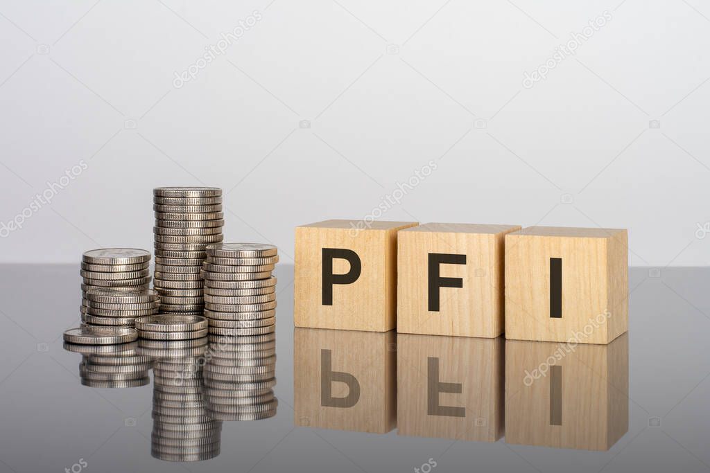pfi. wooden cubes. blocks lie on a black background. stacks with coins. inscription on the cubes is reflected from the surface of the table. selective focus. PFI - short for Private Finance Initiative