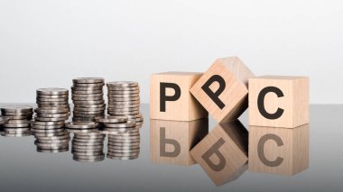 PPC - Pay Per Click - metin, ayna yüzeyinde duran tahta küplerin üzerindeki harflerden oluşur, gri arkaplan. Bozuk paralarla dolu desteler. Yazı yüzeyden yansıtılır.